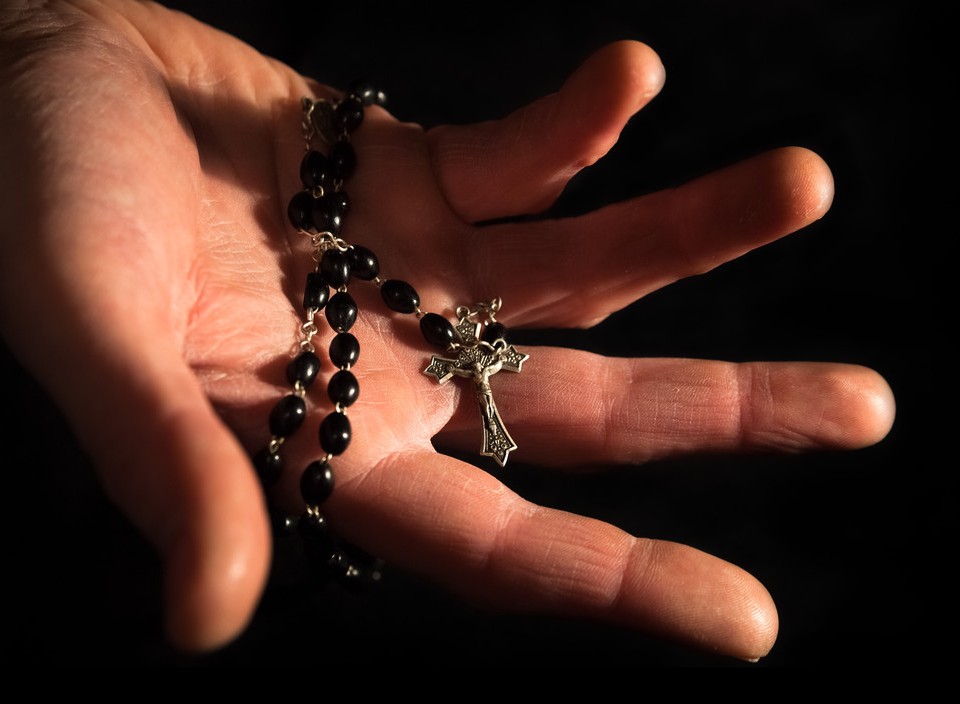 Helping hand holding onto rosary beads and cross.